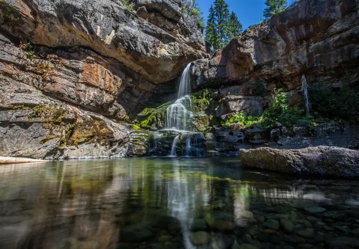 Cascadas en León, agua cristalina cae sobre rocas cubiertas de musgo, reflejándose en un estanque sereno.