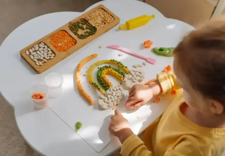 Dziecko tworzy tęczę z plasteliny i ziaren. Powstaje kolorowa zabawka sensoryczna diy.