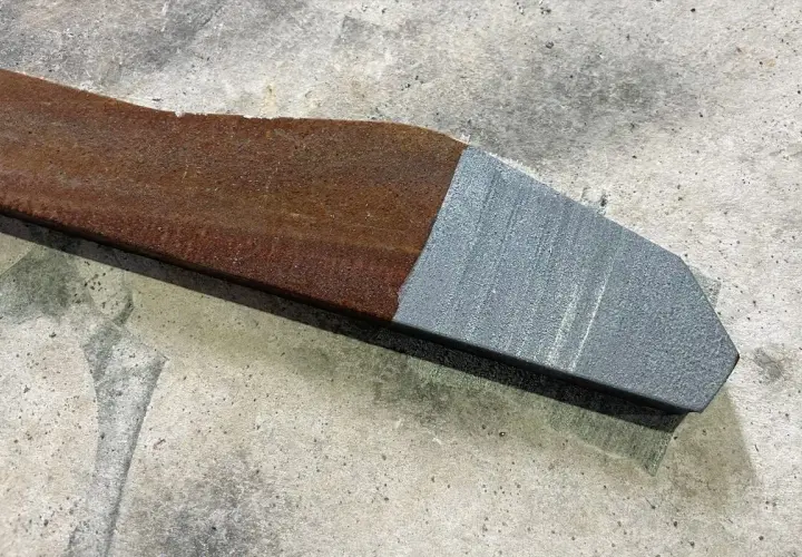 Fragment metalu po jednej stronie zardzewiały, po drugiej idealnie czysty dzięki czyszczeniu laserowemu.