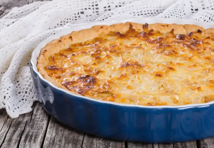 Quiche lorraine dorée dans un plat bleu. Le temps de cuisson et la température parfaits pour un délice croustillant.
