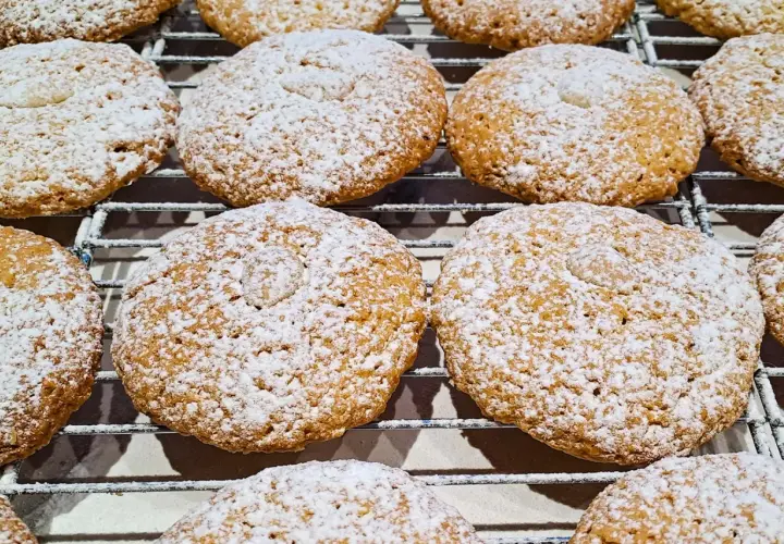Biscotti con farina di mandorle, cosparsi di zucchero a velo, riposano su una griglia.