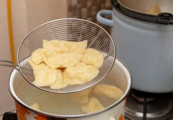 Gotowanie pierogów: cedzak z pierogami nad garnkiem z wrzącą wodą. Tak, pierogi wrzuca się do gotującej wody.