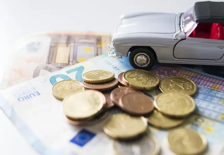 Modellino d'auto su banconote e monete euro. Un promemoria dei costi di gestione, incluso il **super bollo auto**.