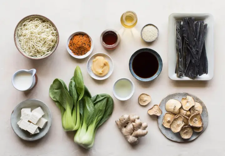 A collection of ingredients for a Japanese meal, including noodles, bok choy, tofu, ginger, dried mushrooms, and various Japanese sauces and seasonings.