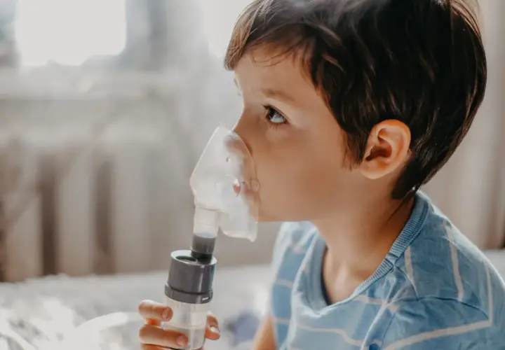 Chłopiec z maską inhalatora na twarzy, wdycha sól fizjologiczną do inhalacji.