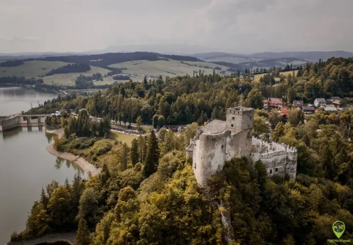 Zamek w Niedzicy góruje nad jeziorem i lasami. W oddali widać góry.