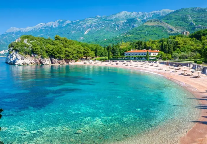 Malownicza zatoka z turkusową wodą i piaszczystą plażą. W tle hotel i zielone wzgórza. Idealne czarnogóra plaże na wakacje.
