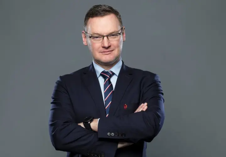 Miłosz Stępiński w granatowym garniturze, z rękami skrzyżowanymi na piersi, patrzy pewnie w obiektyw.