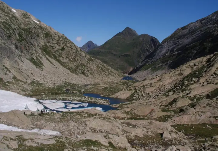 Paisaje de montaña con lagos glaciares y restos de nieve. El pico Mulleres se alza majestuoso en el horizonte.