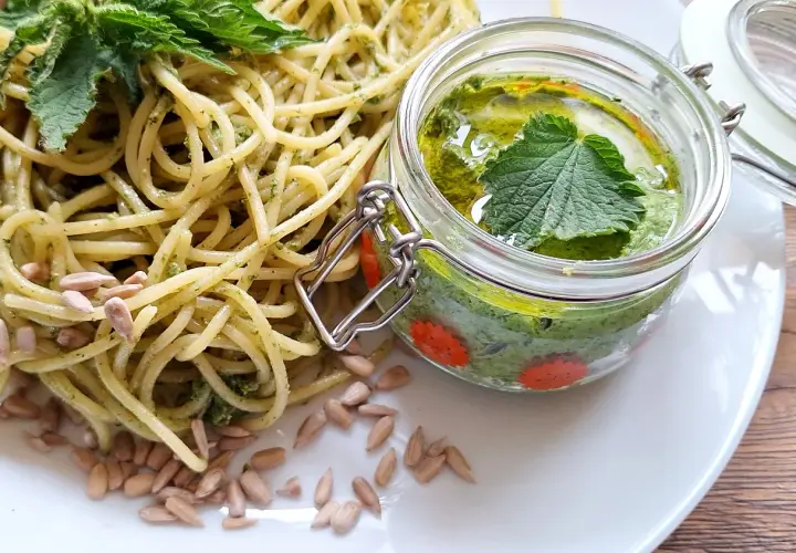 Makaron z domowym pesto z pokrzywy, ozdobiony świeżymi liśćmi i pestkami słonecznika. Pesto w słoiczku wygląda apetycznie.