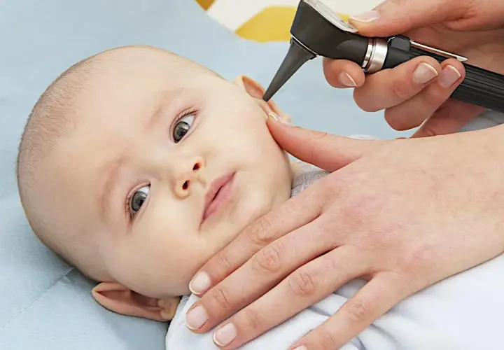 Un medico esamina l'orecchio di un neonato con un otoscopio. È importante controllare i bambini per l'otite.