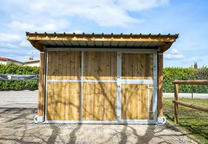 Ein mobiler Pferdestall ohne Baugenehmigung, aus Holz und Metall, mit Dach und Türen, ideal für flexible Pferdeunterbringung.