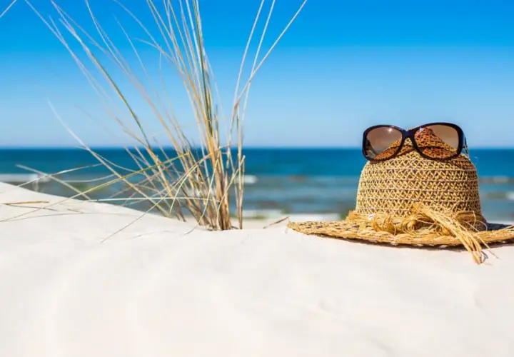 Słomkowy kapelusz z okularami przeciwsłonecznymi na piaszczystej plaży, idealny na wyjazd gdzie nad morze.