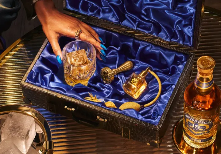 Skutki zbyt niskiej temperatury serwowania: dlaczego nie mrozić whisky. Elegancki zestaw z butelką Chivas Regal 18, szklanką z lodem i złotymi akcesoriami.