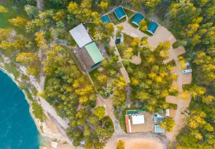 Malowniczy camping w Małopolsce nad turkusową wodą. Domyki, budynki i samochody wśród jesiennych drzew.