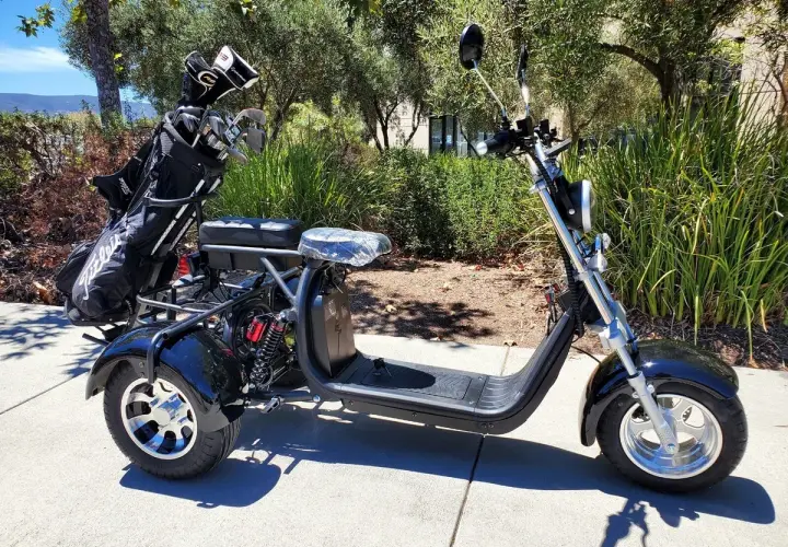 Trike negro de 3 ruedas con bolsa de golf en la parte trasera, aparcado en una acera.