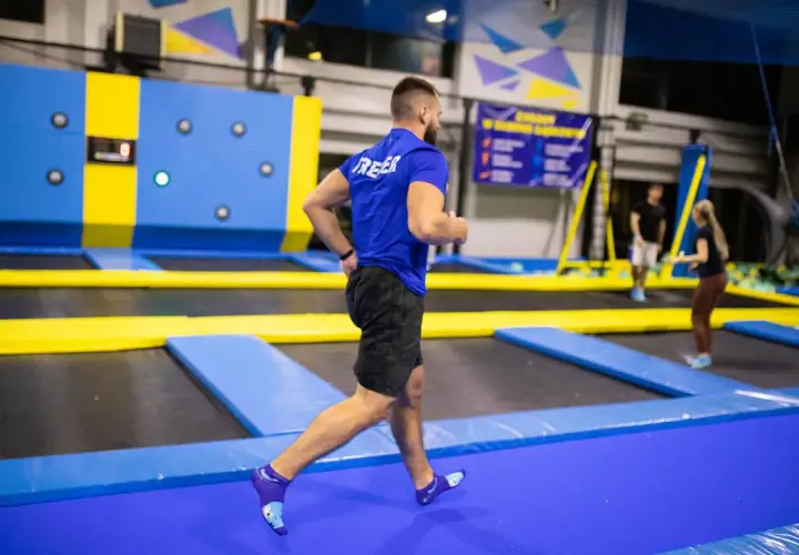 Mężczyzna w niebieskiej koszulce wykonuje trening interwałowy na trampolinach.