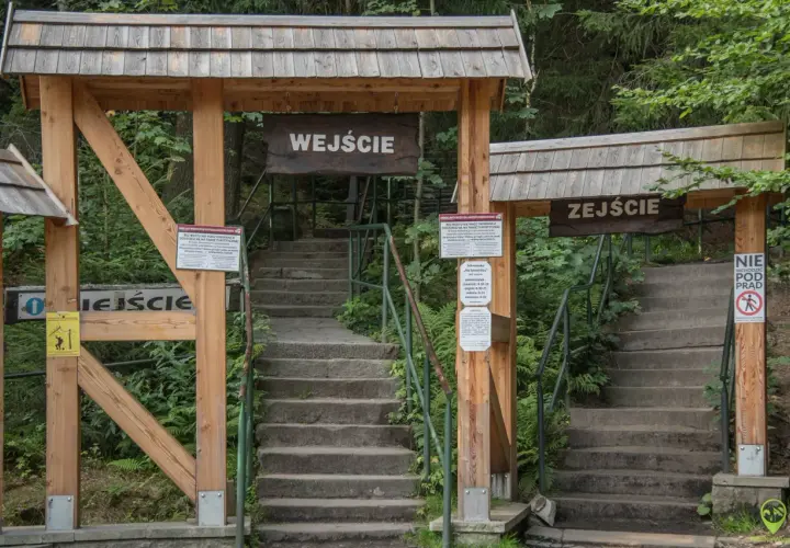 Kamienne schody prowadzą do wejścia na **Szczeliniec Wielki**. Drewniane bramy z tablicami informacyjnymi zapraszają do zwiedzania.