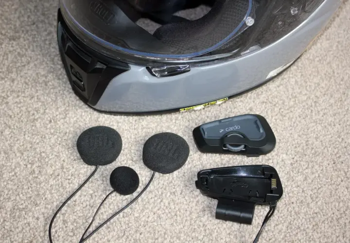 Akcesoria do interkomu motocyklowego Cardo i słuchawki JBL leżą obok kasku. Dowiedz się, jak zamontować interkom do kasku.