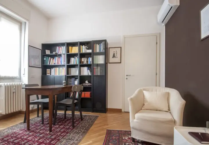 Arredamento accogliente per uno studio di psicoterapia: poltrona comoda, libreria piena e un tavolo per le sedute.