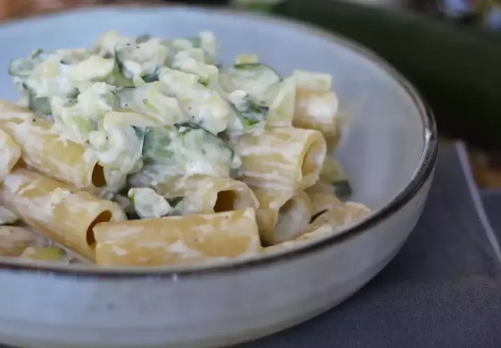 Pasta con calabacín cremosa, servida en un cuenco. Los trozos de calabacín se mezclan con la pasta y una salsa blanca.