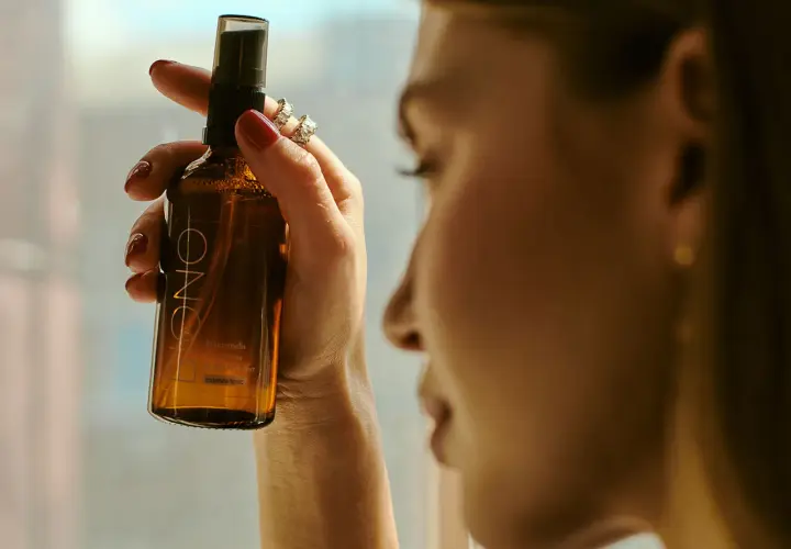 Kobieta trzyma buteleczkę z mgiełką, która zawiera alkohol cetylowy. Delikatna pielęgnacja dla skóry.