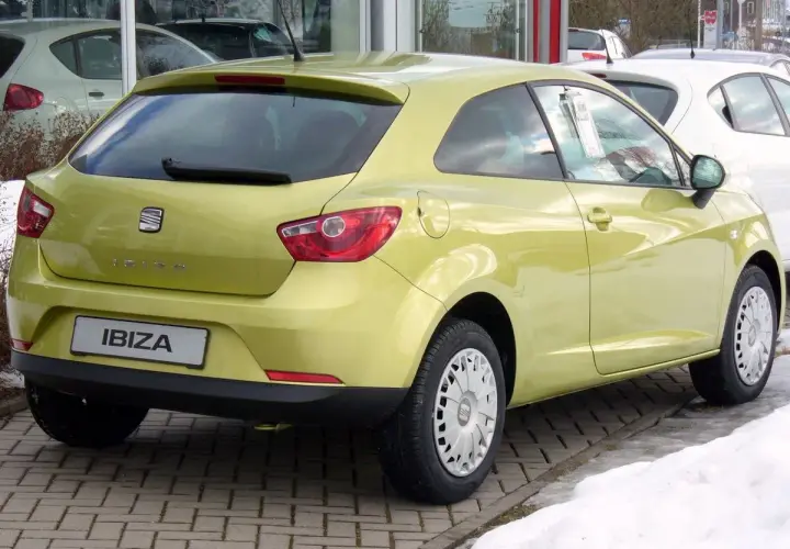 Jasnożółty Seat Ibiza 1.4 benzyna z tyłu, zaparkowany na kostce brukowej, obok śniegu.