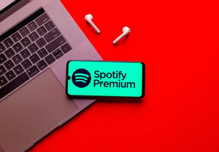Laptop, telefon z logo Spotify Premium i słuchawki na czerwonym tle.