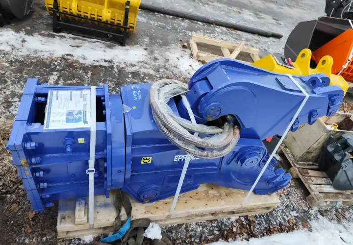 Solidne nożyce hydrauliczne do koparki, gotowe do pracy. W tle żółte i pomarańczowe łyżki.