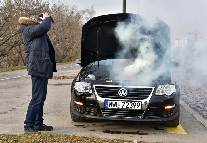 Mężczyzna zrezygnowany patrzy na dym spod maski i czuje zapach spalenizny. Awaria Volkswagena na poboczu.