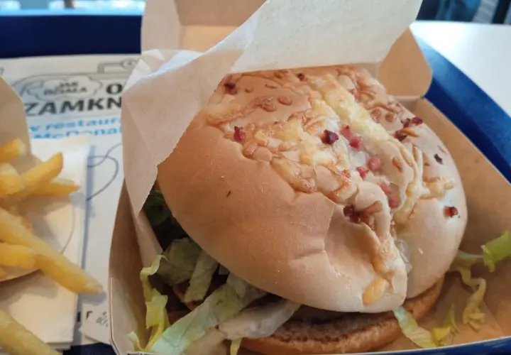 Pyszny lumberjack burger z McDonald's w papierowym opakowaniu, obok złociste frytki.