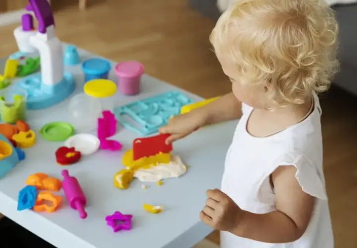 Mała blondynka w żłobku tworzy cuda z plasteliny. Wesołe zabawy sensoryczne rozwijają jej kreatywność.