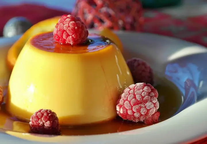 Crème aux œufs onctueuse, nappée de caramel et garnie de framboises givrées. Un délice visuel et gustatif.
