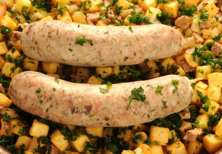 Deux andouillettes au four, dorées et savoureuses, reposent sur un lit de pommes de terre sautées et de persil frais. Un plat réconfortant prêt à être dégusté.