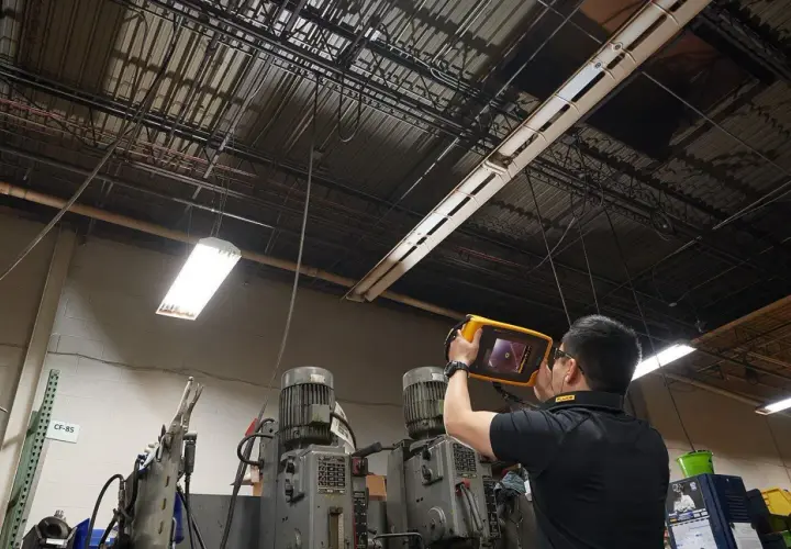 Técnico revisa el techo de una fábrica con un dispositivo para detectar una fuga de aire.