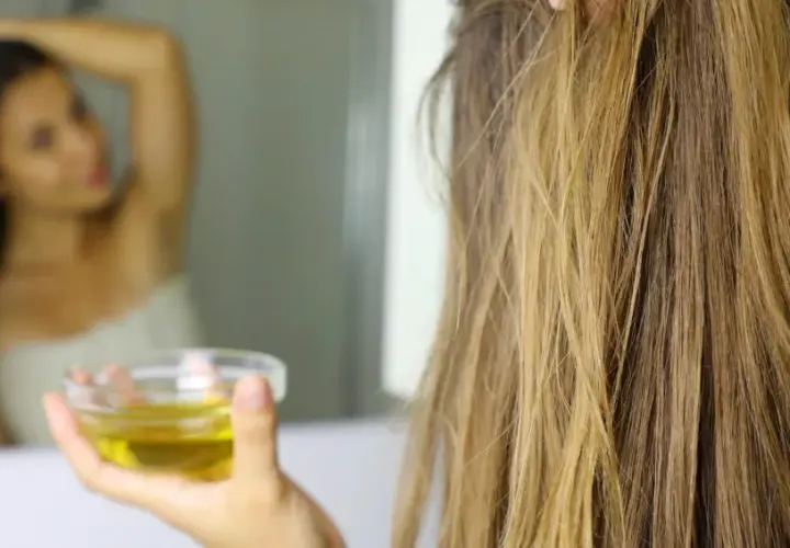 Mujer se aplica aceite de oliva en el cabello, demostrando que el aceite de oliva es bueno para el pelo.