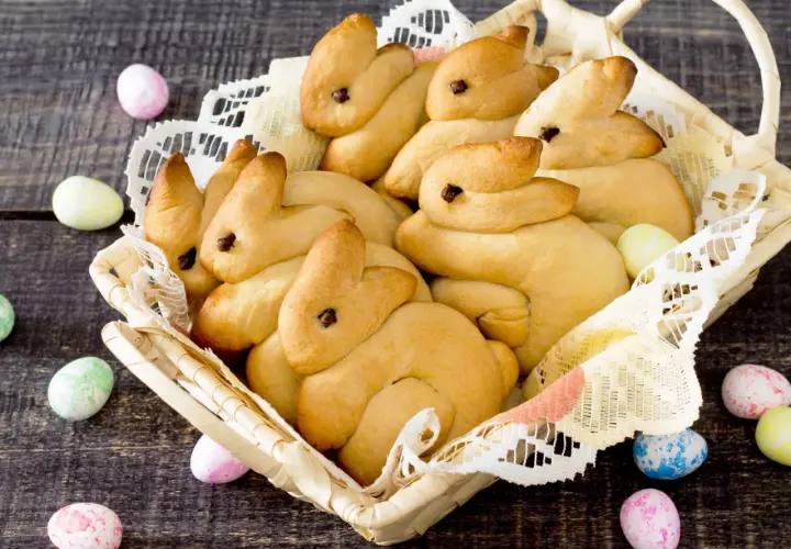 Korb voller goldbrauner Quark Osterhasen, umgeben von bunten Ostereiern auf dunklem Holz.