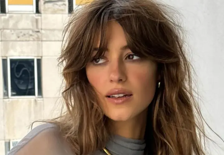 Mujer con flequillo cortina desfilado, cabello castaño ondulado y mirada pensativa.