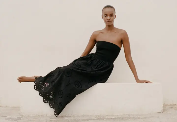 Mujer con vestido negro sin tirantes y falda larga con bordados florales, un ejemplo de moda ecológica.