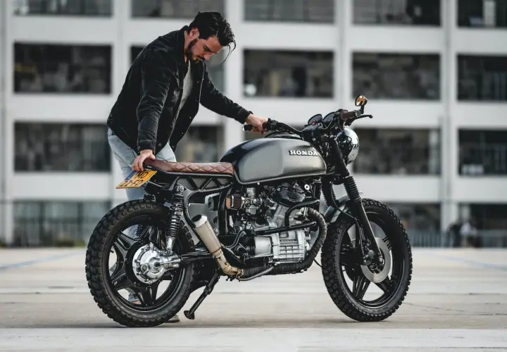 Uomo con moto custom grigia. La sella in pelle marrone ha una **godronatura** a rombi.