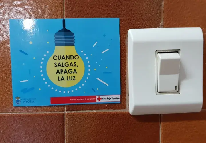 Un cartel azul con una bombilla amarilla y el texto "CUANDO SALGAS, APAGA LA LUZ" junto a un interruptor blanco.