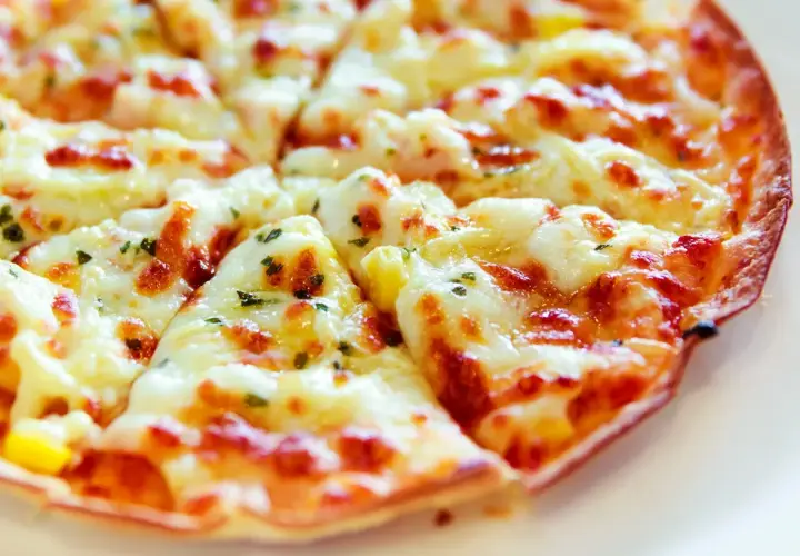 Pyszna pizza z tortilli, obficie posypana serem i ziołami, pokrojona na trójkątne kawałki.