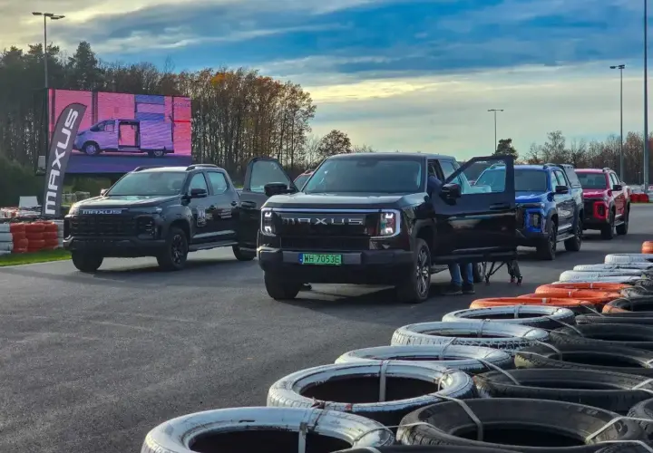 Kolekcja nowoczesnych pickupów Maxus, w tym czarny model z otwartymi drzwiami, ustawiona na torze wyścigowym.
