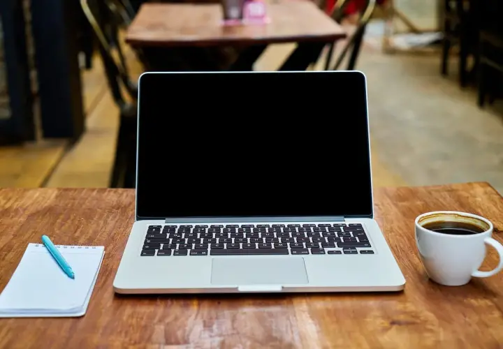 Laptop z pustym ekranem, notatnik z długopisem i filiżanka kawy na drewnianym stole. Idealne miejsce do pracy nad projektem z wykorzystaniem dysku hybrydowego.