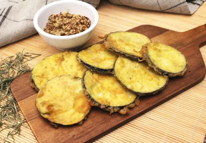 Berenjenas rebozadas doradas y crujientes, servidas en tabla de madera con un cuenco de mostaza.