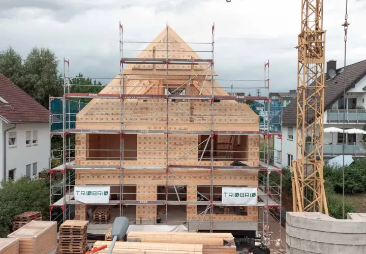 Holzbau im Wohngebiet: Ein Haus aus Holz wird mit Gerüsten und Kran errichtet.