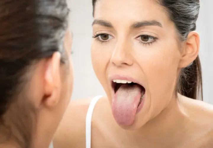 Mujer revisa su lengua en el espejo, buscando una lengua sana.