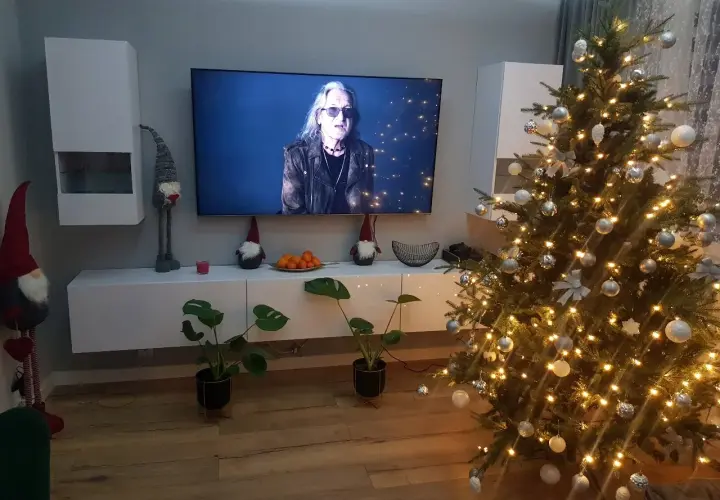 Świąteczny nastrój w domu: choinka, ozdoby, krasnale i telewizor z koncertem.