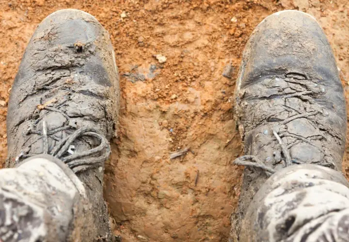 Mud-caked boots stand in dirt. The question "do boots shrink over time?" lingers as these boots look like they've seen many adventures.