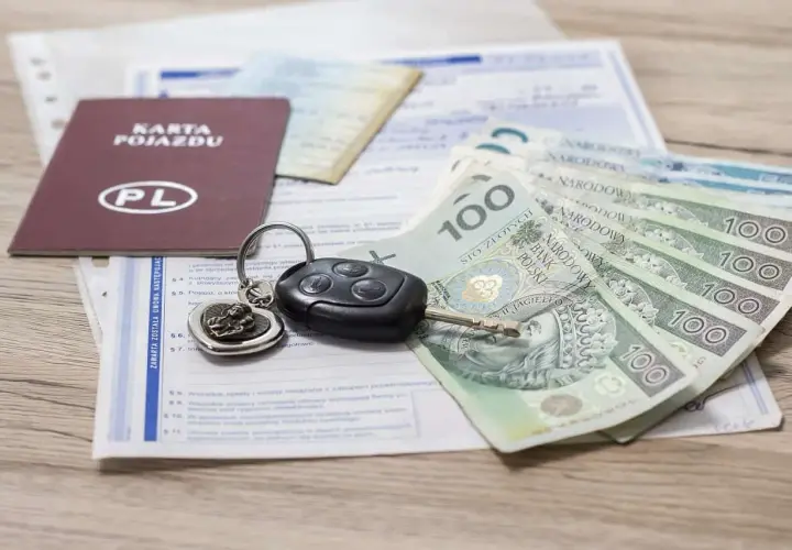 Karta pojazdu, kluczyki i polskie banknoty 100 zł leżą na dokumentach. Gotowy do zakupu lub sprzedaży samochodu.
